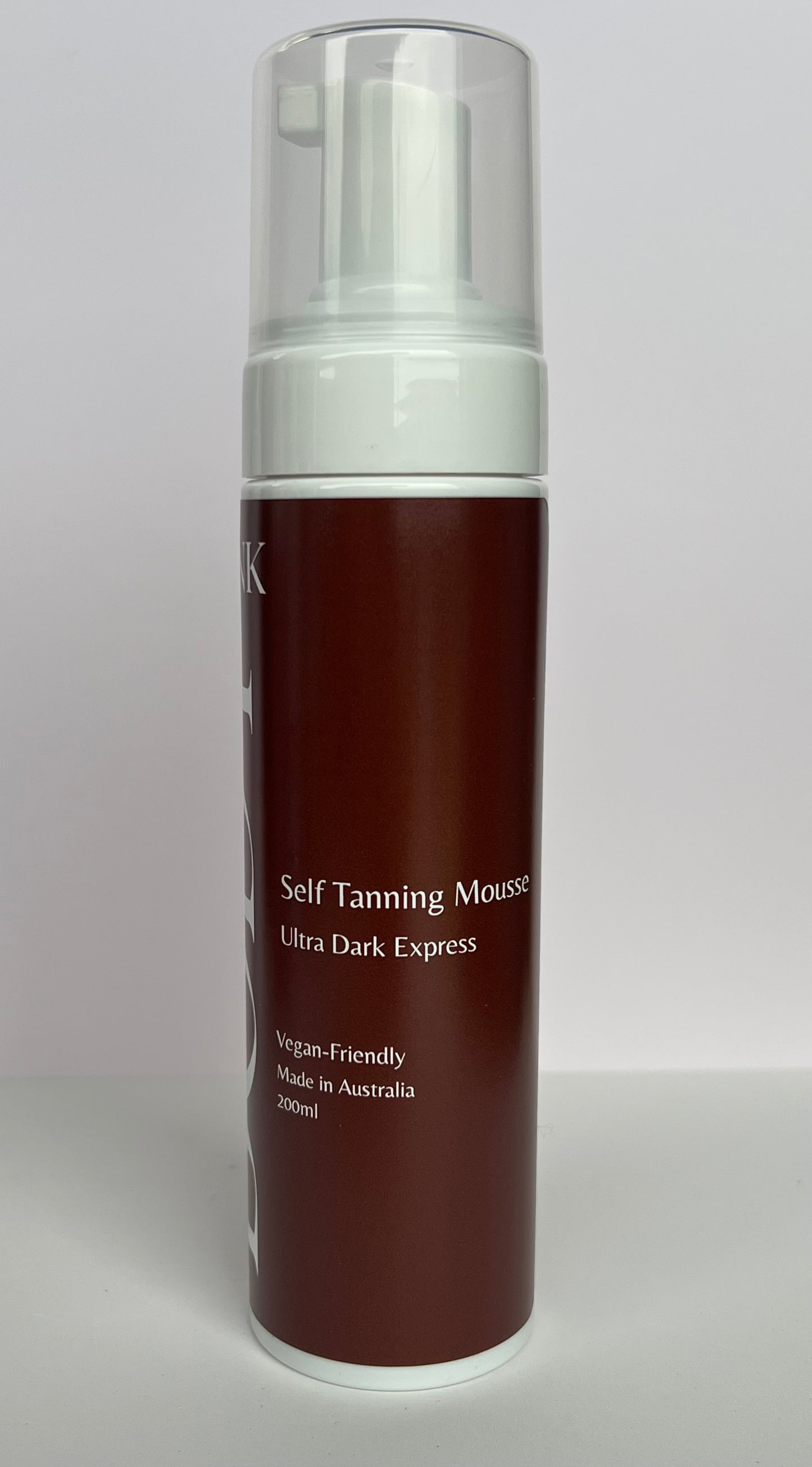 Self tanning mousse bottle with brown body and white cap on a light gray background
