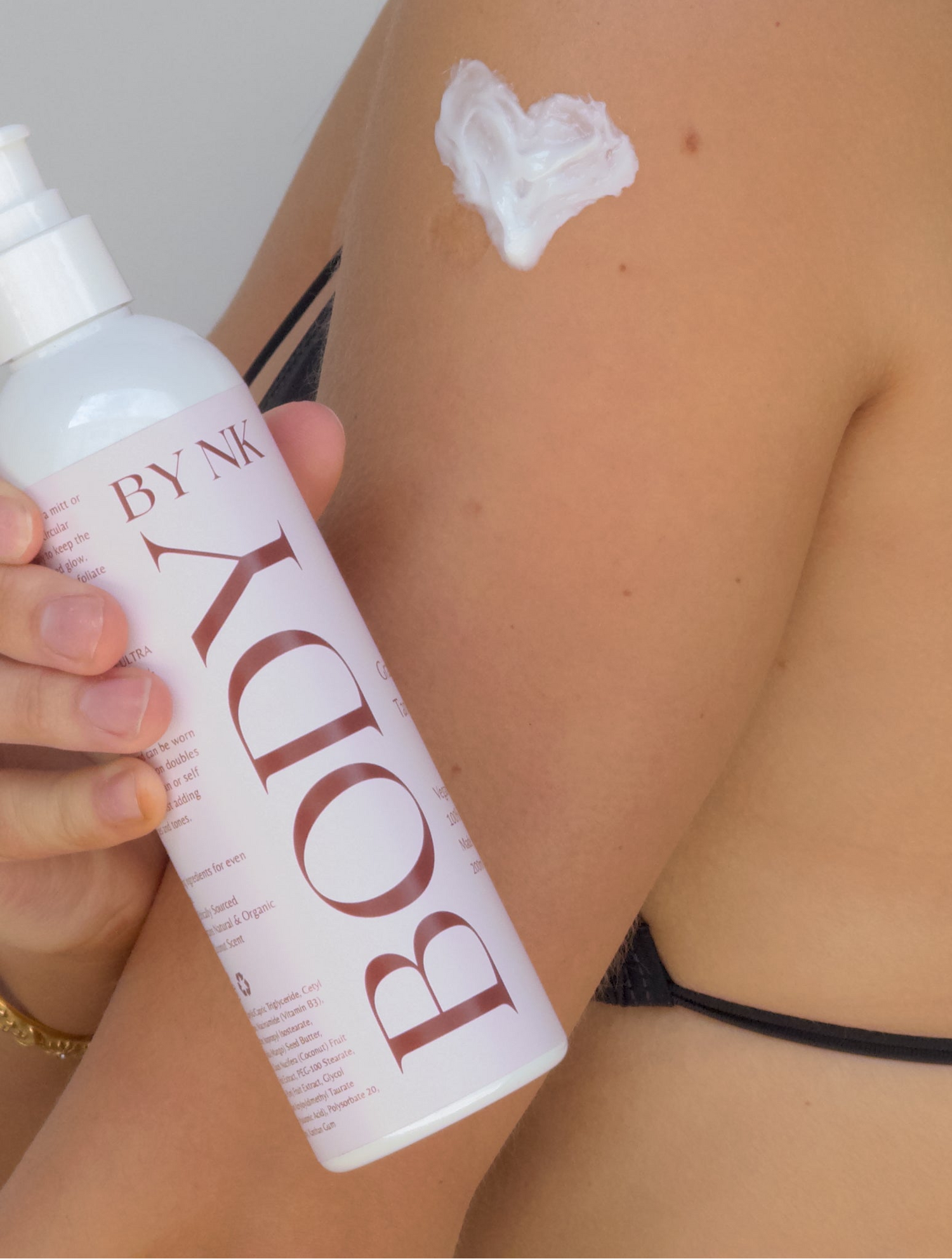 Person holding a BODY BY NIK bottle with a small amount of cream on their skin.