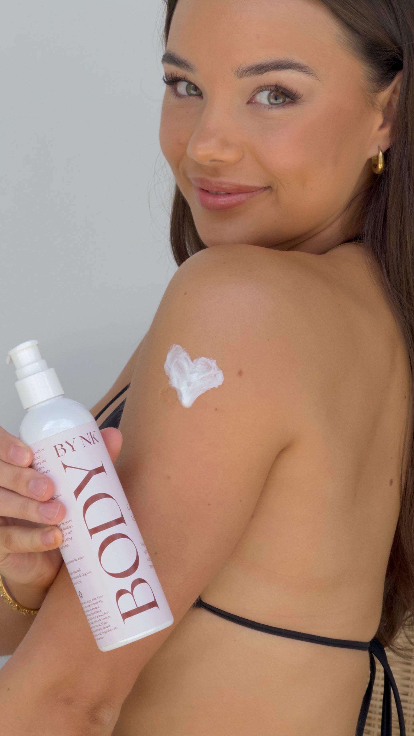Woman applying sunscreen with a bottle labeled 'BODY' on a plain background