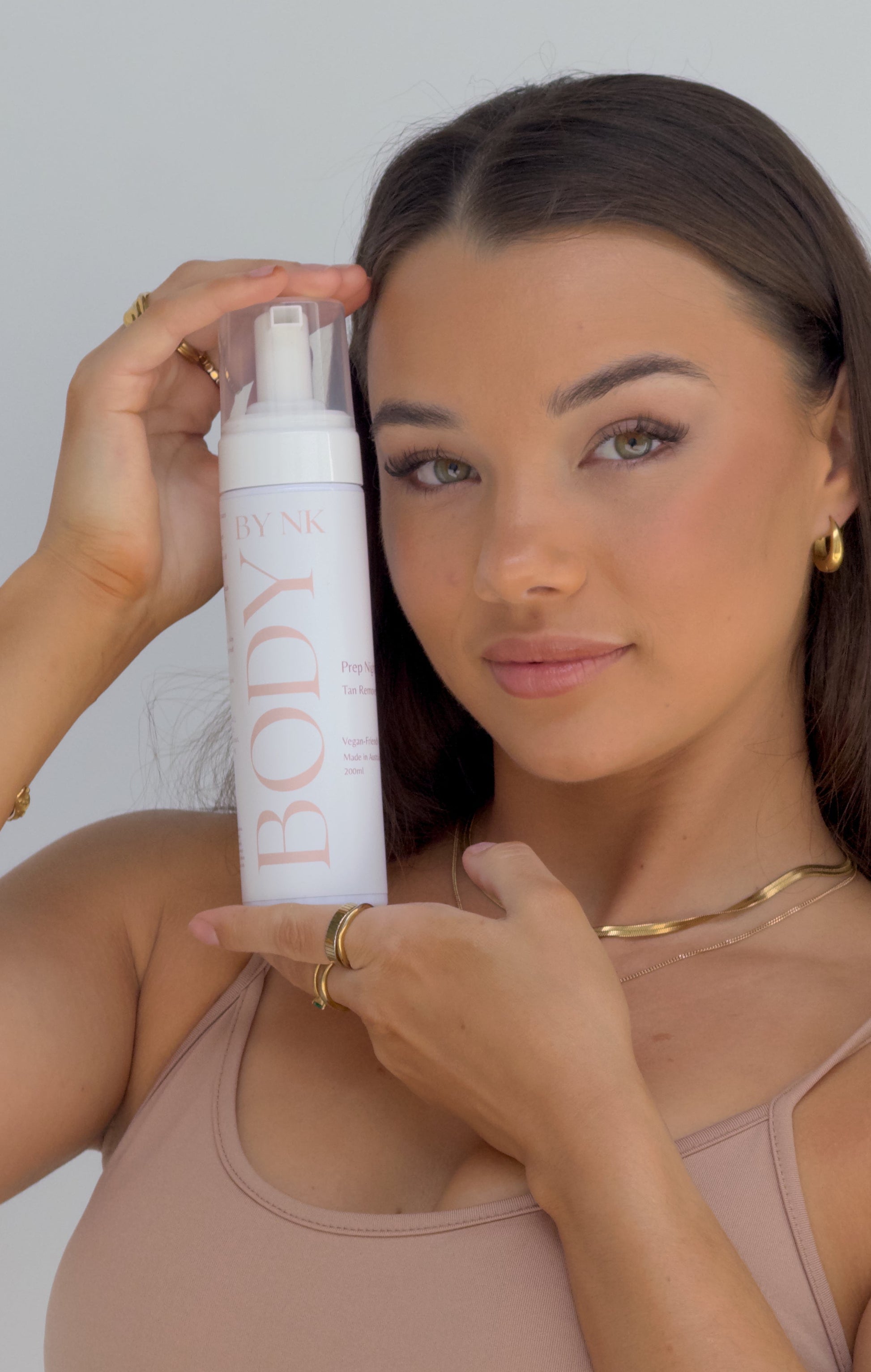 Woman holding a bottle of 'BODY by NK' 2 in 1 tan eraser product