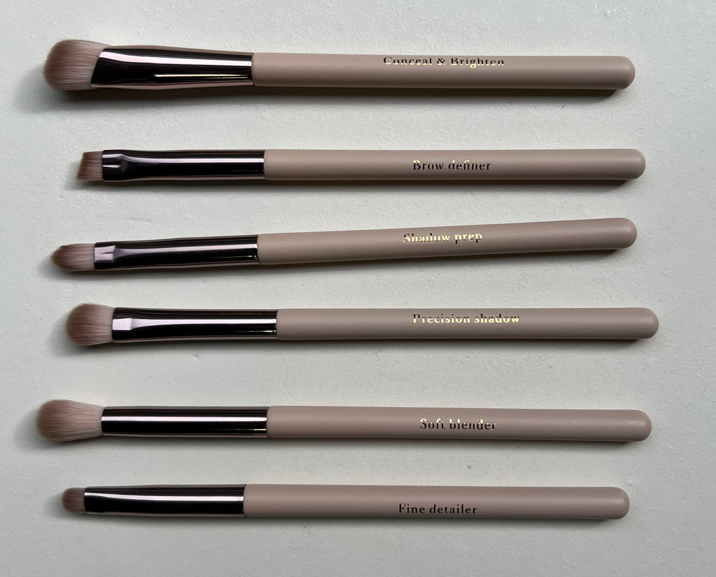 Set of makeup brushes with beige handles and black ferrules on a light gray surface.