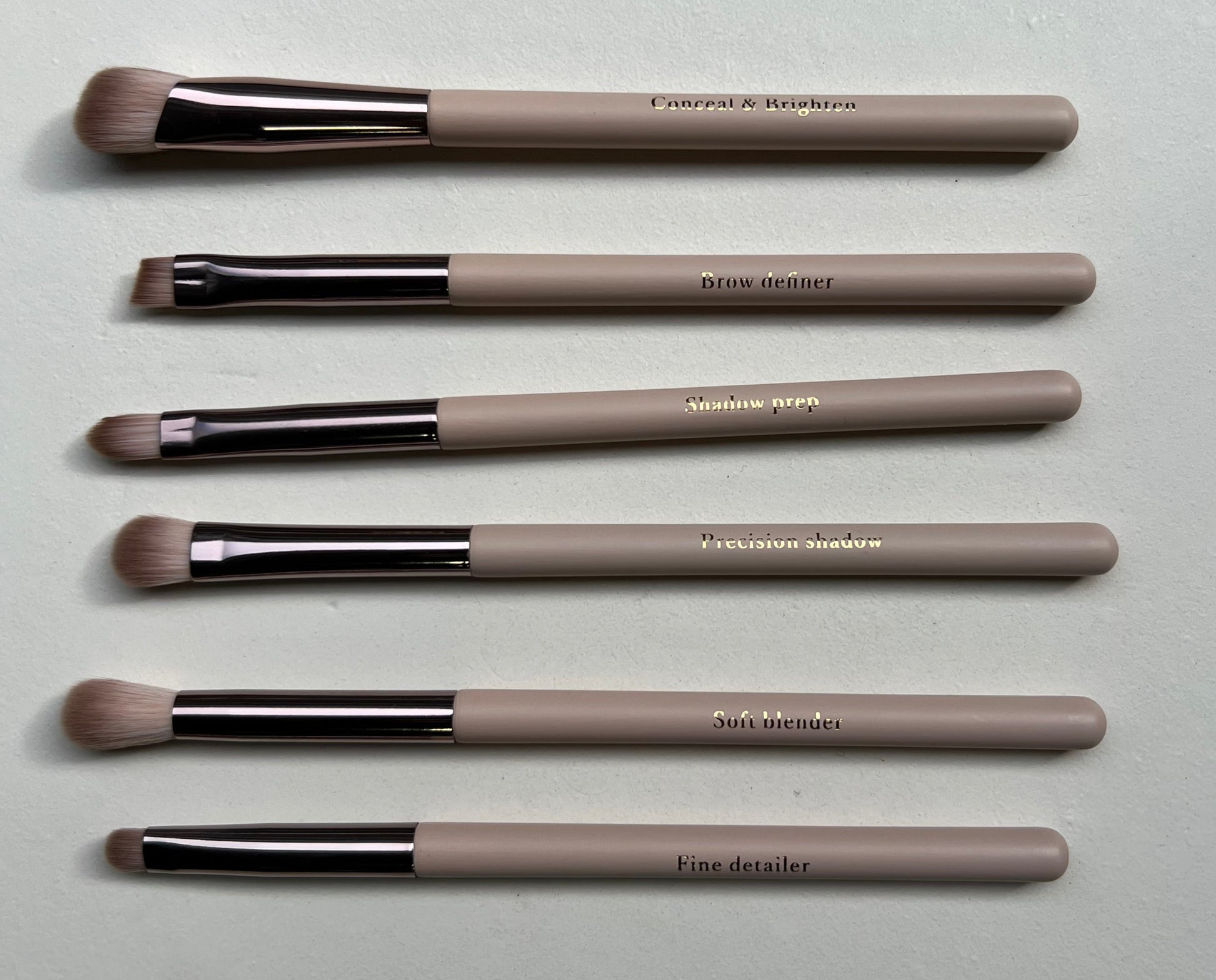 Set of makeup brushes with beige handles and black ferrules on a light gray surface.