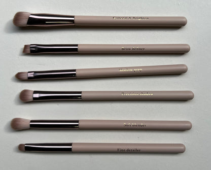 Set of makeup brushes with beige handles and black ferrules on a light gray surface.