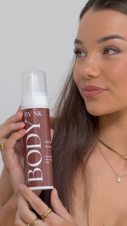 Woman holding a 'BY NK BODY' product against a plain background